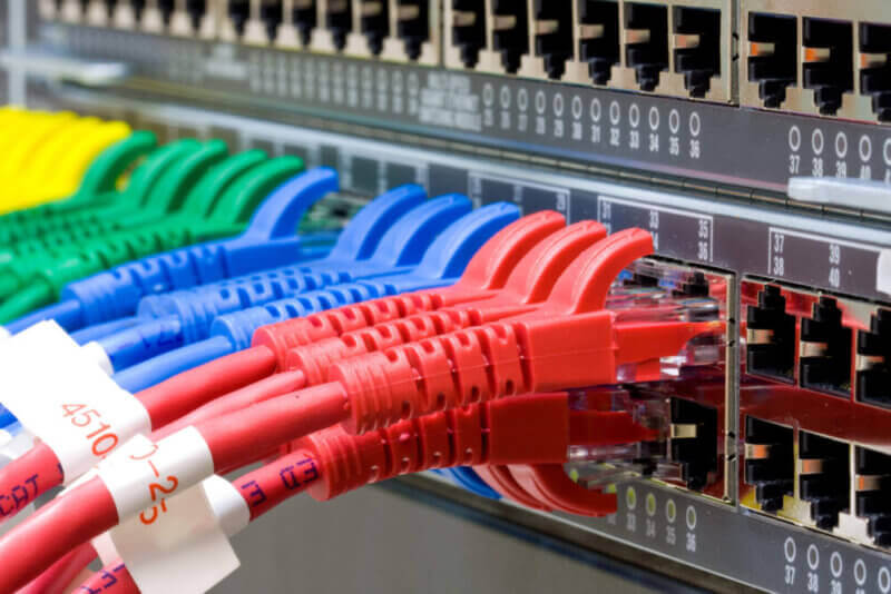 IT Network Management Red, blue, green and yellow patch cables connected to a network switch
